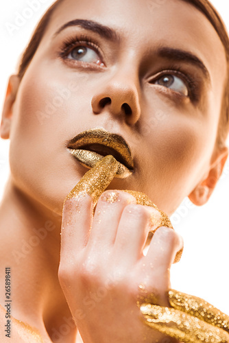 young beautiful woman with golden makeup and sparkles on fingers touching lips and looking away isolated on white