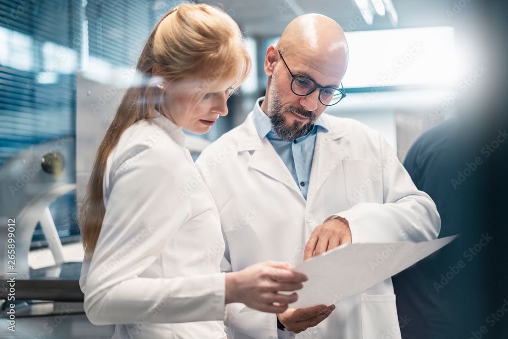 Two technicians wearing lab coats looking at plan Two technicians wearing lab coats looking at plan