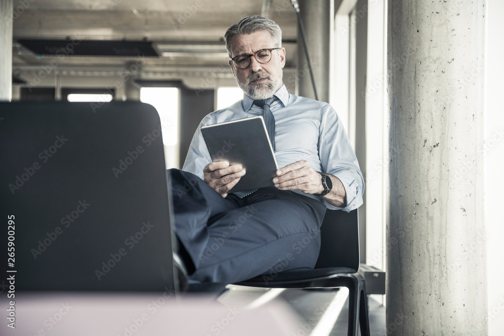 Mature businessman sitting on chair using tablet Mature businessman sitting on chair using tablet