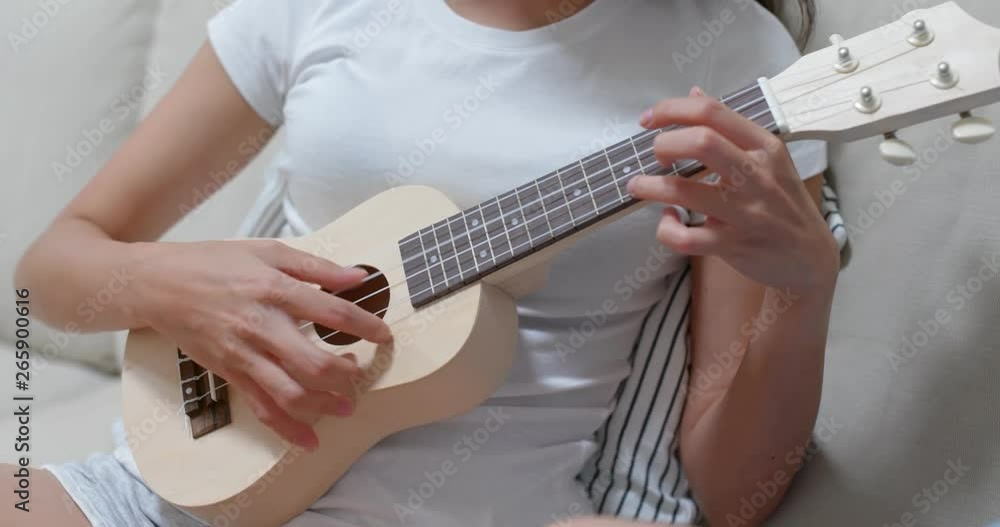 Woman practice ukulele and sit on sofa at home Woman practice ukulele and sit on sofa at home