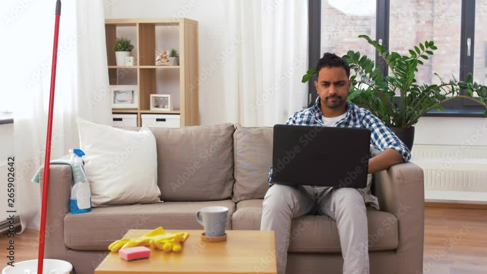 household, housework and technology concept - indian man with laptop computer, mop and bucket after home cleaning household, housework and technology concept - indian man with laptop computer, mop and bucket after home cleaning