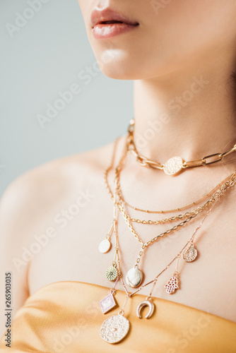 cropped view of young woman with shiny lips in golden necklaces isolated on grey