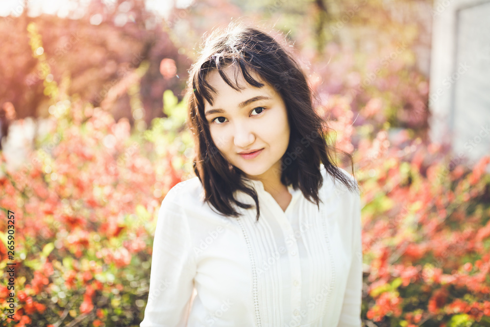 Cheerful asian young woman in a white blouse in a blooming park. Cheerful asian young woman in a white blouse in a blooming park.