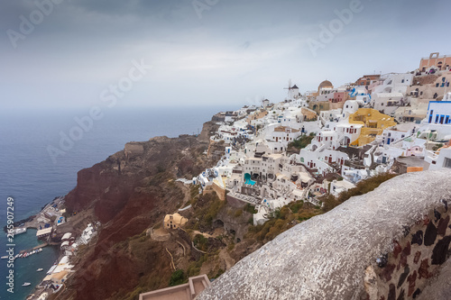 View of colorful houses of Oia and red cliffs on a rainy day