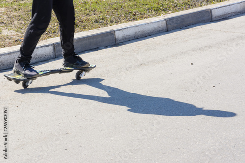 Man riding a waveboard on the asphalt. Type of skateboard in the road and the feet of a man. Shadow on the pavement.