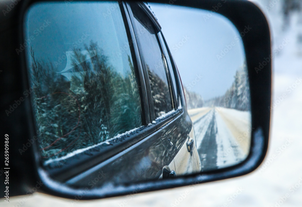 Winter forest highway at the automobile rear-view mirror