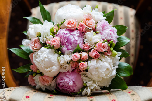 Beautiful bouquet of peonies, pink roses and freesias, against the background of the chair, top view