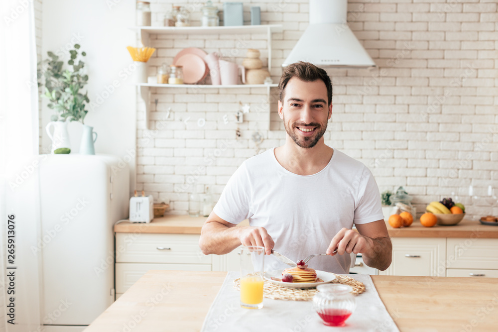 smiling bearded man in white t-shirt eating pancakes in kitchen smiling bearded man in white t-shirt eating pancakes in kitchen