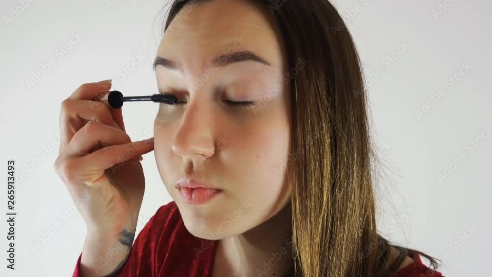 A young brunette woman in a red blouse does makeup, paints her eyes. She looks in the mirror. Close-up A young brunette woman in a red blouse does makeup, paints her eyes. She looks in the mirror. Close-up