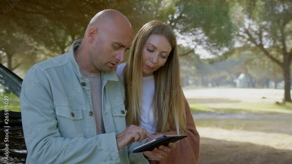 Couple discussing route on digital tablet. Happy young man and woman leaning at car and using tablet computer with navigation app. Technology concept Couple discussing route on digital tablet. Happy young man and woman leaning at car and using tablet computer with navigation app. Technology concept