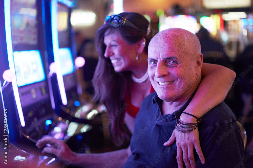 portrait of elderly gambler couple playing slot machine in casino