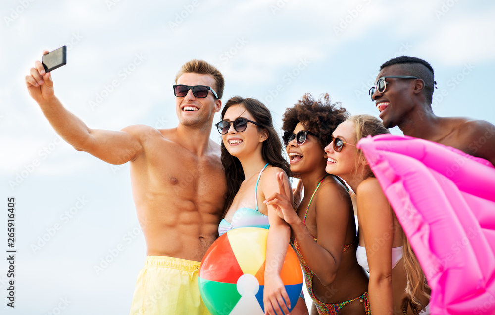 friendship, summer holidays and people concept - group of happy friends taking picture by smartphone on selfie stick on beach