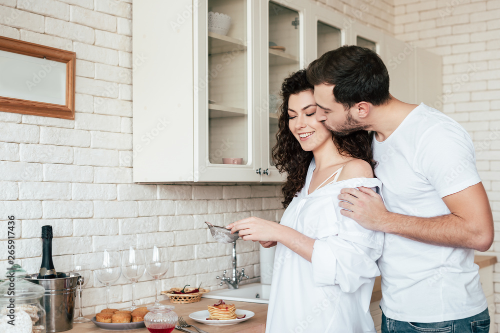 man kissing girlfriend while she preparing breakfast in kitchen man kissing girlfriend while she preparing breakfast in kitchen