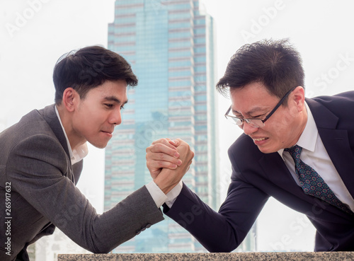 Fotografi Two businessman are clashed arm wrestle on the marble table front of skyscraper
