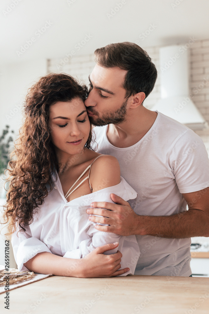 bearded man embracing and kissing girlfriend in kitchen bearded man embracing and kissing girlfriend in kitchen