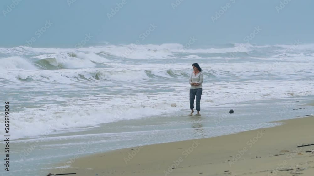 Attractive woman walking the beach with bad stormy weather - looking at the sea. Slow motion people footage. Attractive woman walking the beach with bad stormy weather - looking at the sea. Slow motion people footage.