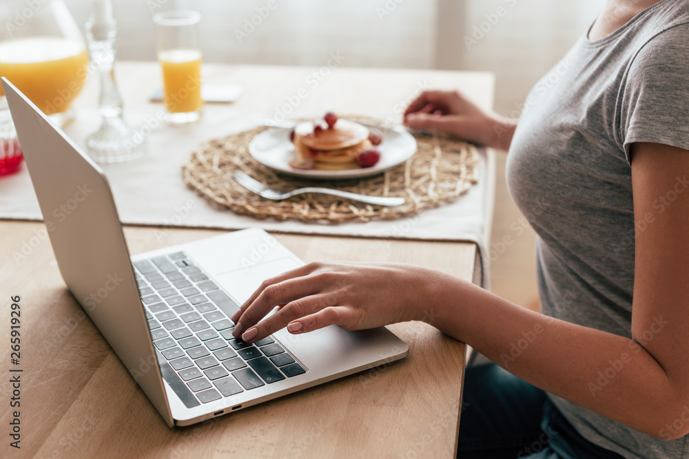 partial view of woman using laptop during breakfast partial view of woman using laptop during breakfast