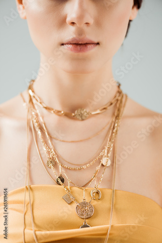 partial view of young woman with shiny lips in golden necklaces isolated on grey