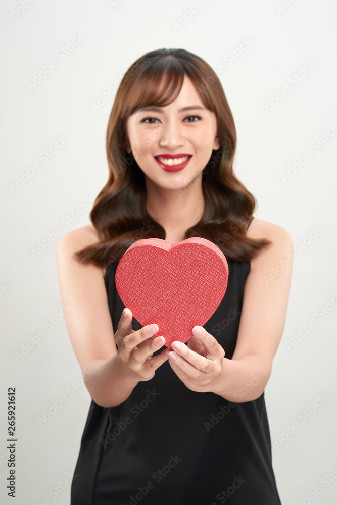 Cute young woman holding pink heart symbol against pale white background Cute young woman holding pink heart symbol against pale white background