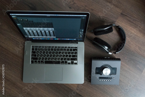 Flat lay of sound designers tools on dark wood table: laptop with mixing scene, sound card, headphones, microphone. Sound engineering tools. Professional sound card for music mixing and mastering