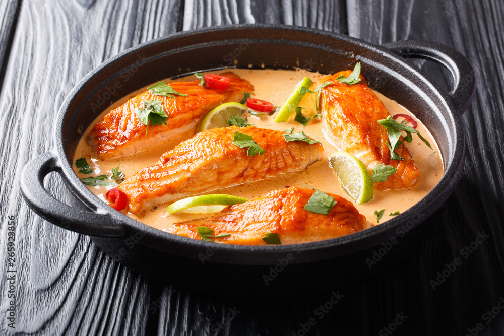 Asian cuisine. Salmon with coconut sauce, lime and herbs close-up in a pan on the table. horizontal