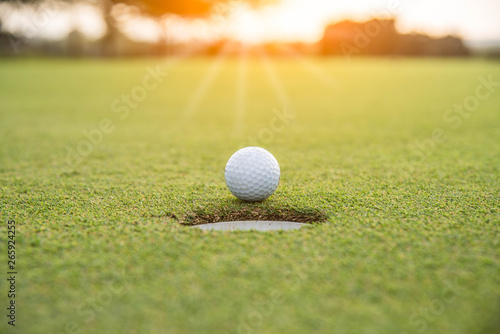 Golf ball putting on green grass near hole golf to win in game at golf course with blur background and sunlight ray