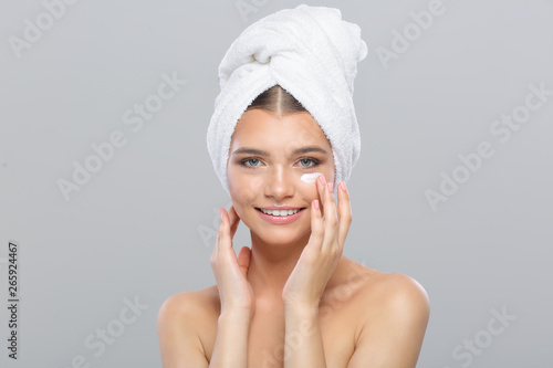 Beautiful young girl with a towel on her head uses face cream