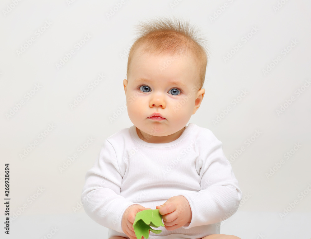 Charming blue-eyed baby sitting on a white background with colored educational toys Charming blue-eyed baby sitting on a white background with colored educational toys