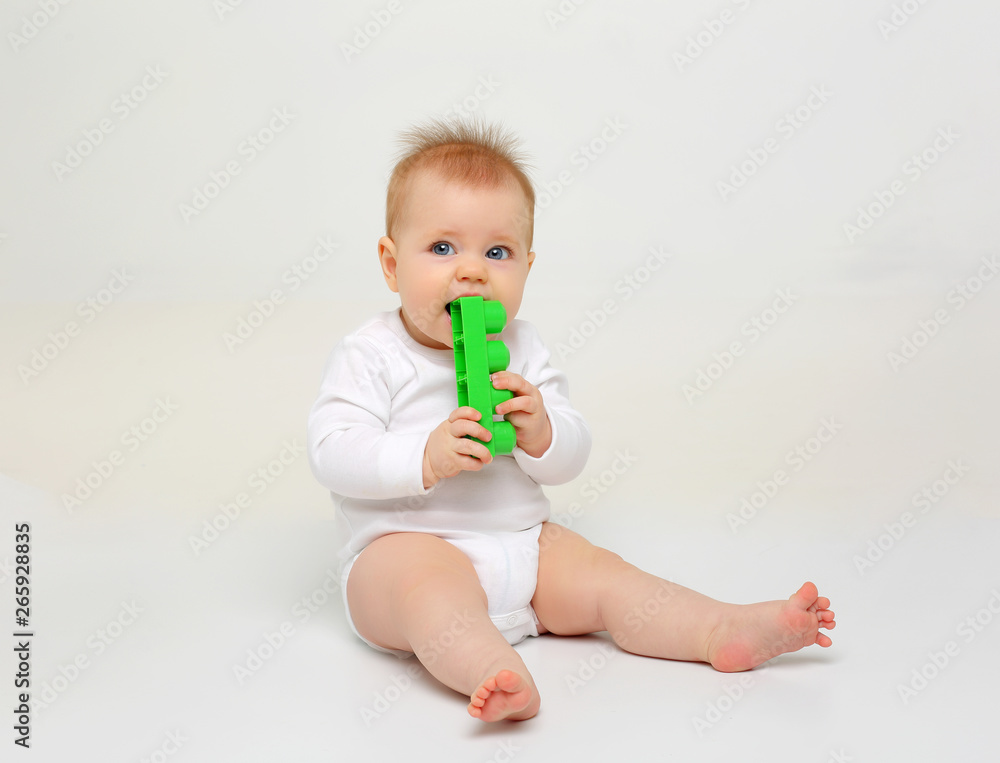 Charming blue-eyed baby sitting on white background and nibbling toys Charming blue-eyed baby sitting on white background and nibbling toys