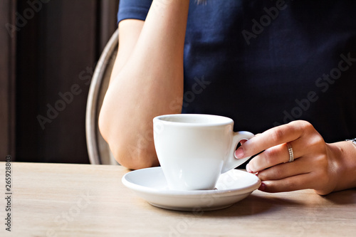 A cup of coffee in a cafe and a girl's hands.