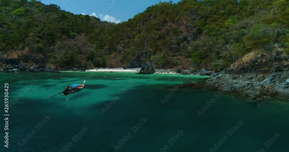 Aerial: A lone longtail boat stands near the beach with turquoise water. Aerial: A lone longtail boat stands near the beach with turquoise water.