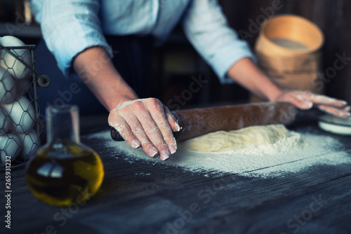Female hands making dough in ball shape. Basic homemade dough with ingredients on the side on wooden table with natural light. Home healthy food. Selective focus. Focus on the dough.
