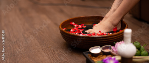 Closeup shot of a woman feet dipped in water with petals in a wooden bowl