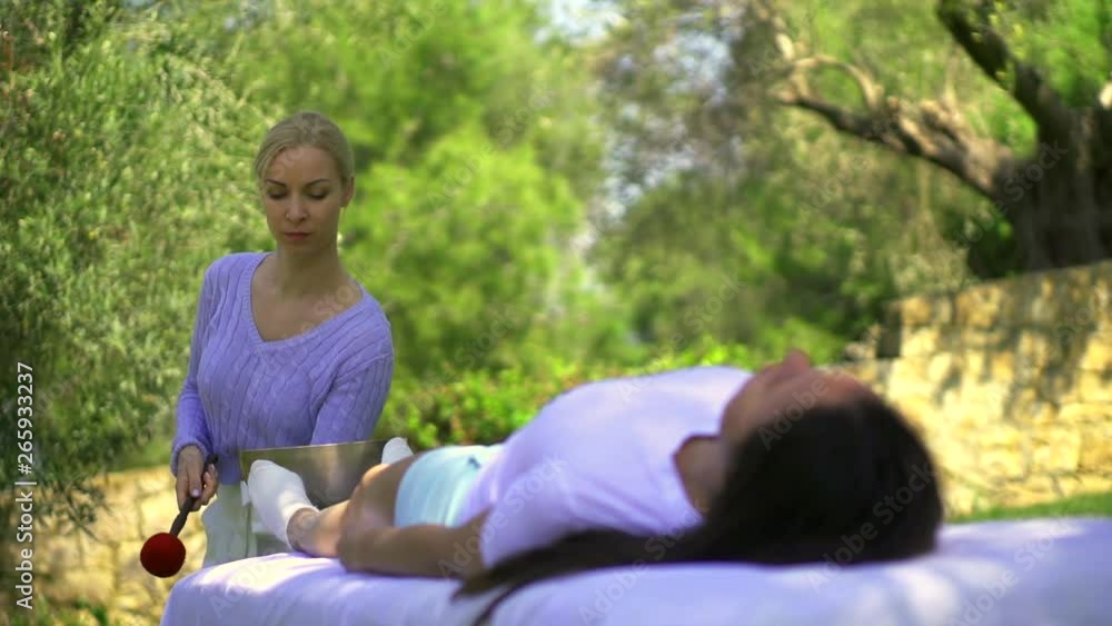 One girl is lying in the open air, and the second makes her massage sound vibrations using the bowl. One girl is lying in the open air, and the second makes her massage sound vibrations using the bowl.
