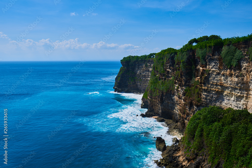 Azure beach with rocky mountains and clear water with huge waves of Indian ocean at sunny day. View of Uluwatu cliff and blue sea in Bali, Indonesia. Beautiful world, travel, holiday.