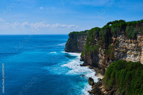 Azure beach with rocky mountains and clear water with huge waves of Indian ocean at sunny day. View of Uluwatu cliff and blue sea in Bali, Indonesia. Beautiful world, travel, holiday.