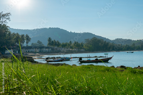 A beautiful scenic gulf of Thailand on sunny day with clear blue sky at Khanom beach with local fisherman boats on scene mountain on background green grass and tree on foreground. 