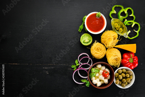 Ingredients for cooking pasta. Dry pasta. Mushrooms, sausages, tomatoes, vegetables. Top view. On a black wooden background. Free copy space.