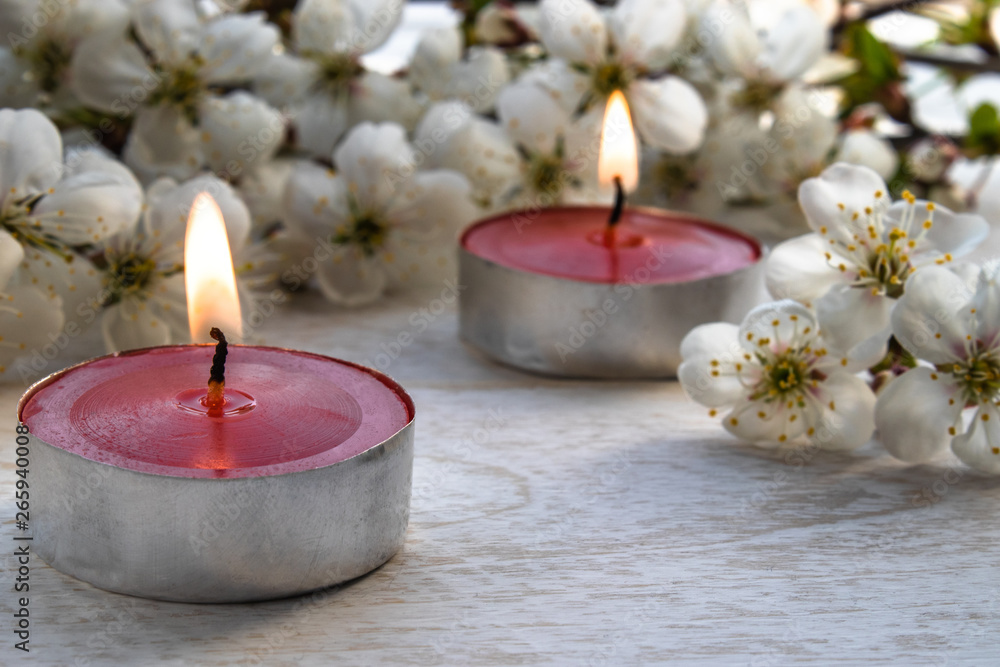 A candle stands on a wooden white table near the branches of white flowers of cherry. A candle stands on a wooden white table near the branches of white flowers of cherry.