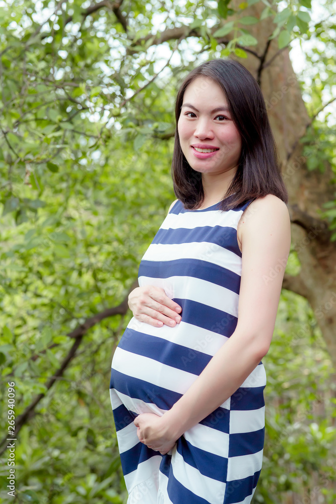A pretty Asian woman is pregnant. Wearing a striped shirt Stand to rest in the garden happily. A pretty Asian woman is pregnant. Wearing a striped shirt Stand to rest in the garden happily.