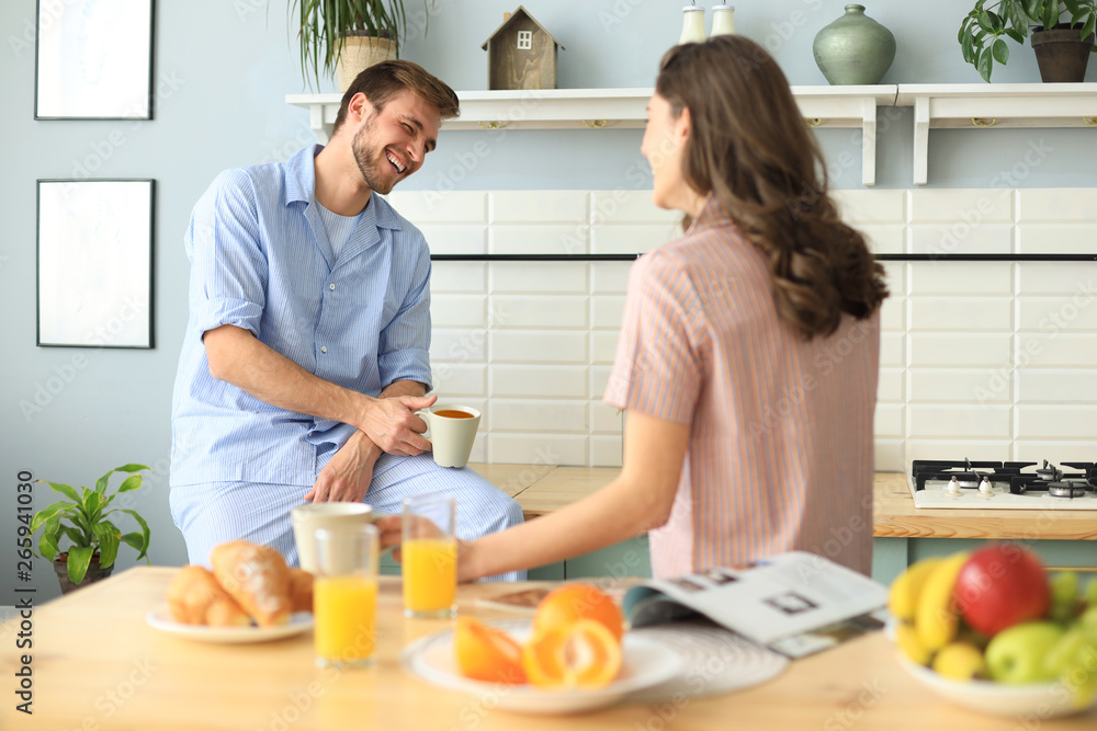 Beautiful young couple in pajamas is looking at each other and smiling while cooking in kitchen at home. Beautiful young couple in pajamas is looking at each other and smiling while cooking in kitchen at home.