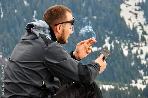 Photography The boy smokes and holds the phone in the mountains against the background of a