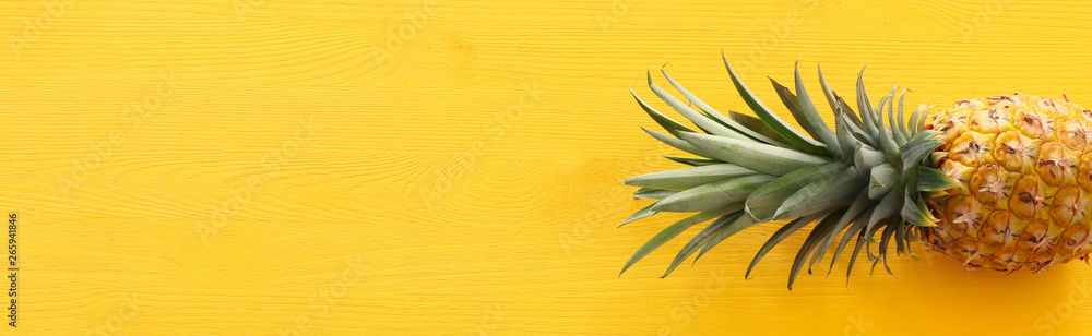 Fototapeta premium Banner of Ripe pineapple over yellow wooden background. Beach and tropical theme. Top view