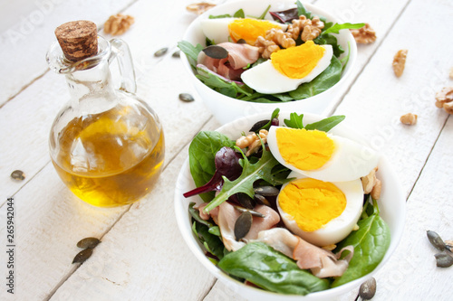 Sałatka z jajkiem, orzechami i szynką parmeńska w białych miskach, w tle oliwa z oliwek