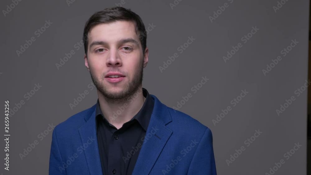 Closeup shoot of young handsome caucasian man showing thumb up looking at camera with background isolated on gray Closeup shoot of young handsome caucasian man showing thumb up looking at camera with background isolated on gray