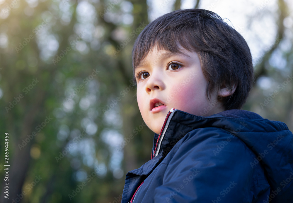 Outdoor portrait of attractive boy sitting in the park, Low view of Kid looking out with blurry trees background in spring or summer. Outdoor portrait of attractive boy sitting in the park, Low view of Kid looking out with blurry trees background in spring or summer.