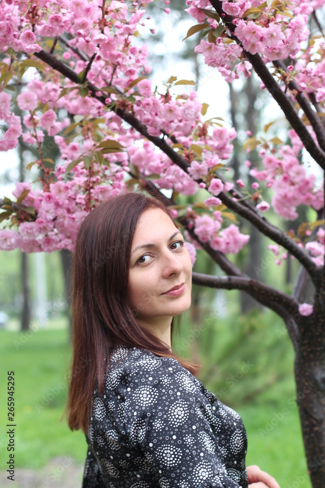 Portrait of beutiful girl in sakura tree. Sakura flowers surround the girl. Sakura branch by her face. Japanese tree