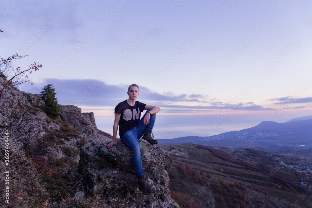 Young attractive man located with  on the top of mountains looks into the distance at sunset
