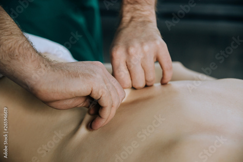 The hands of a male masseur he is doing massage the back of a woman in the lumbar region. skin pulling in