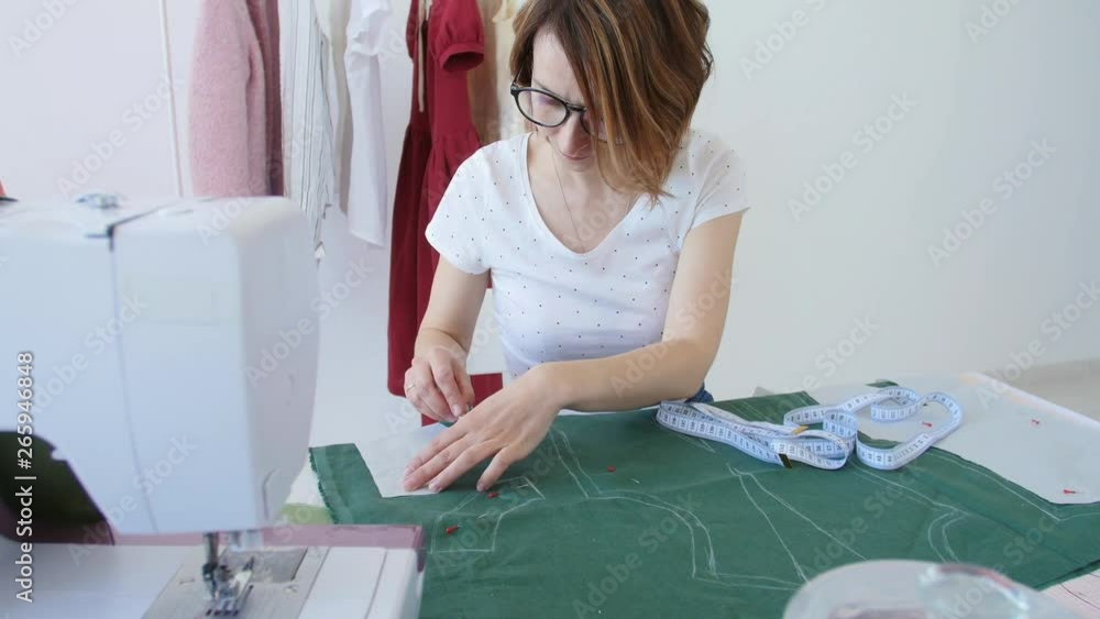 Concept of hobby and small business. Young female designer is designing clothes in a bright studio workshop Concept of hobby and small business. Young female designer is designing clothes in a bright studio workshop